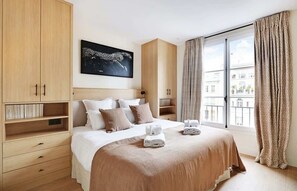 Ein Hotelzimmer mit einem großen Bett, einem Holzschrank und Blick auf Gebäude durch das Fenster.