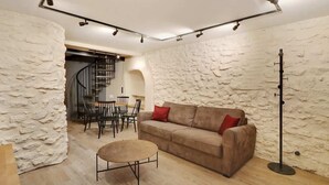 A cozy living room with a stone wall, a brown sofa with red cushions, a round coffee table, and a floor lamp. - A Cosy 1-BR/1BA Duplex in Montmartre (Paris)