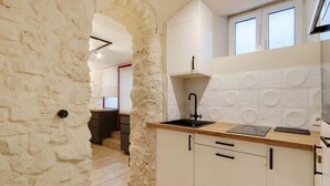 A kitchen with a stone archway, white cabinets, a black faucet, and a wooden countertop. - A Cosy 1-BR/1BA Duplex in Montmartre (Paris)