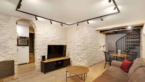 A modern living room with a stone wall, a flat-screen TV, a wooden coffee table, a sofa, and a dining area with a spiral staircase. - A Cosy 1-BR/1BA Duplex in Montmartre (Paris)