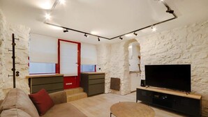A living room with a sofa, a small round table, a TV on a wooden stand, and a stone wall. - A Cosy 1-BR/1BA Duplex in Montmartre (Paris)