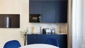 A modern kitchen with dark cabinets, a microwave, a kettle, and a toaster. There is a dining table with chairs and a vase with flowers on the counter. - A Romantic 1-BR with Services in Batignolles (Paris)