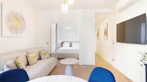 A modern hotel room with a sofa, a round dining table, a TV mounted on the wall, and a hallway leading to a bathroom. - A Romantic 1-BR with Services in Batignolles (Paris)