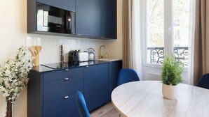 A compact kitchen with dark blue cabinets, a microwave, and a sink. There's a round table with chairs and a potted plant. - A Romantic 1-BR with Services in Batignolles (Paris)