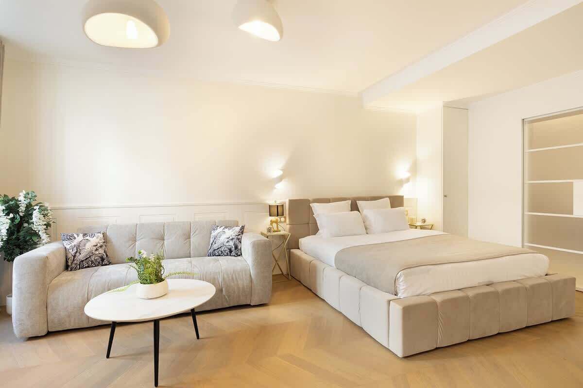 A modern bedroom with a large bed, a sofa, a small table, and a bedside lamp.