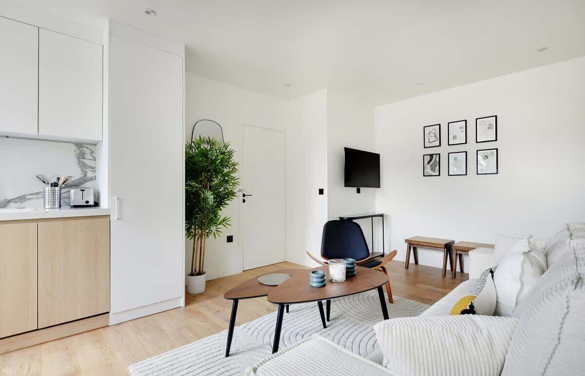 Un salon moderne avec un canapé, une table basse, un téléviseur et des œuvres d’art encadrées accrochées au mur.