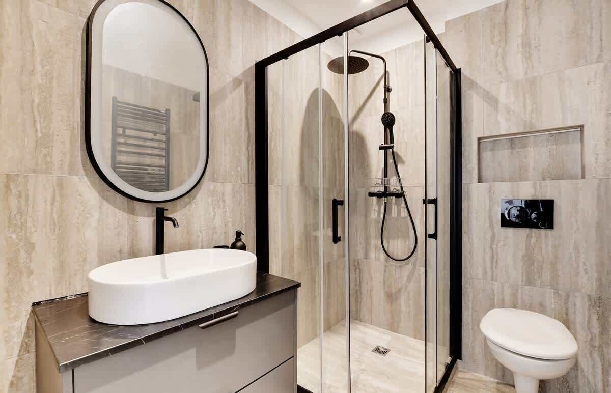 Een moderne badkamer met een douche met glazen wand, een witte wastafel en een toilet.