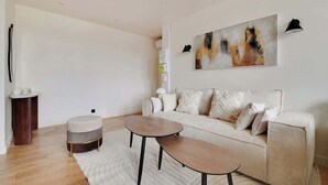 Un soggiorno moderno con un divano color beige, due tavolini rotondi, un tappeto bianco e un grande quadro astratto appeso alla parete.