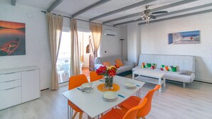 A modern living room with a white sofa, orange chairs, and a dining table set with plates and a vase of flowers. - WELCS APARTMENT 367 EMP with communal pool (Empuriabrava)