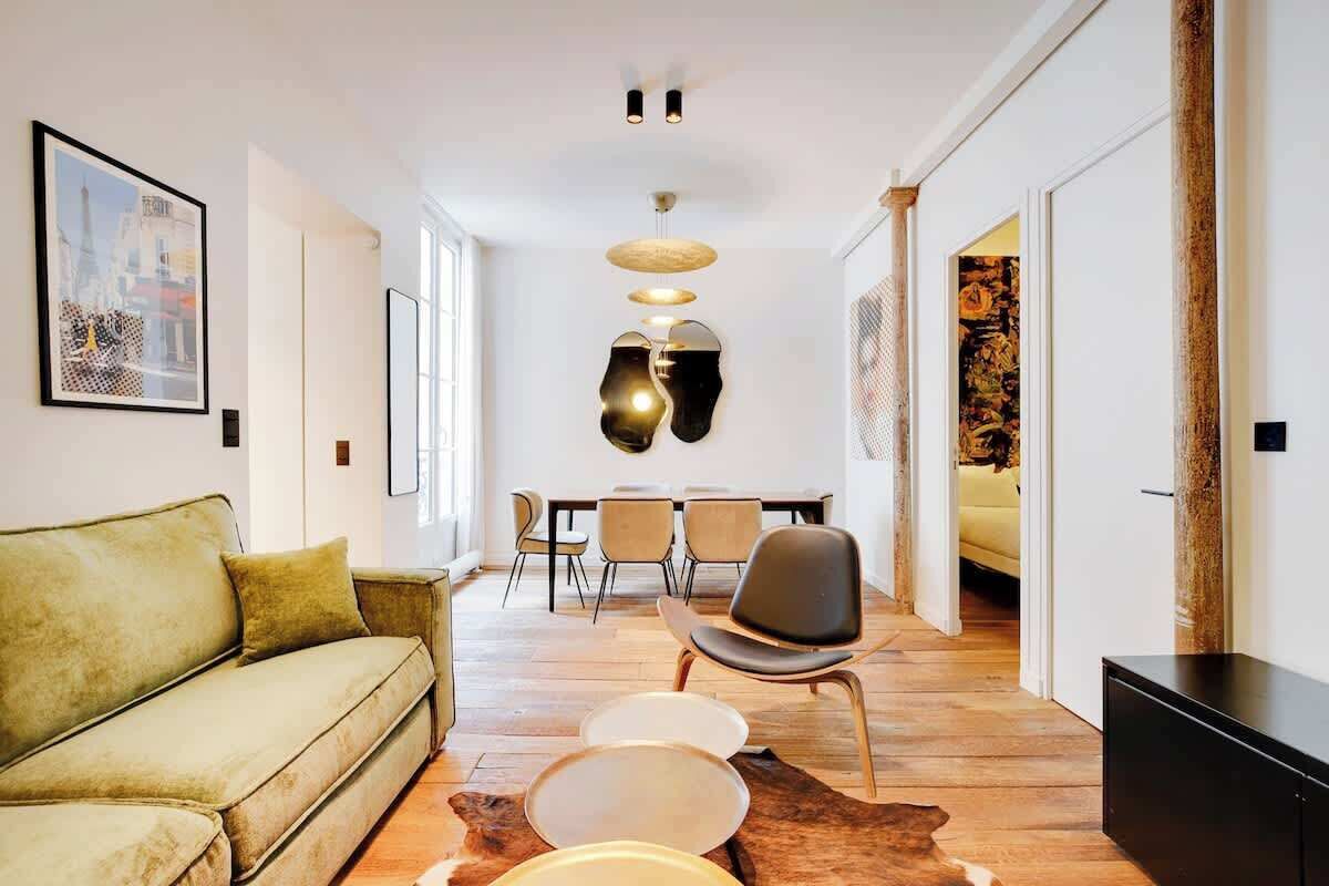A modern living room with a sofa, dining table, chairs, and a unique ceiling light fixture.