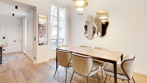 A dining area with a wooden table and four chairs, a large mirror on the wall, and a ceiling light fixture. - A Fancy 2-BR/1Ba - Montorgueil (Paris)