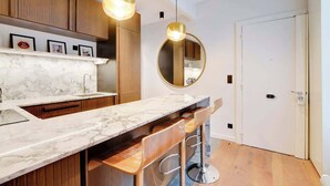 A modern kitchen with marble countertops, wooden cabinets, and two pendant lights. - A Fancy 2-BR/1Ba - Montorgueil (Paris)