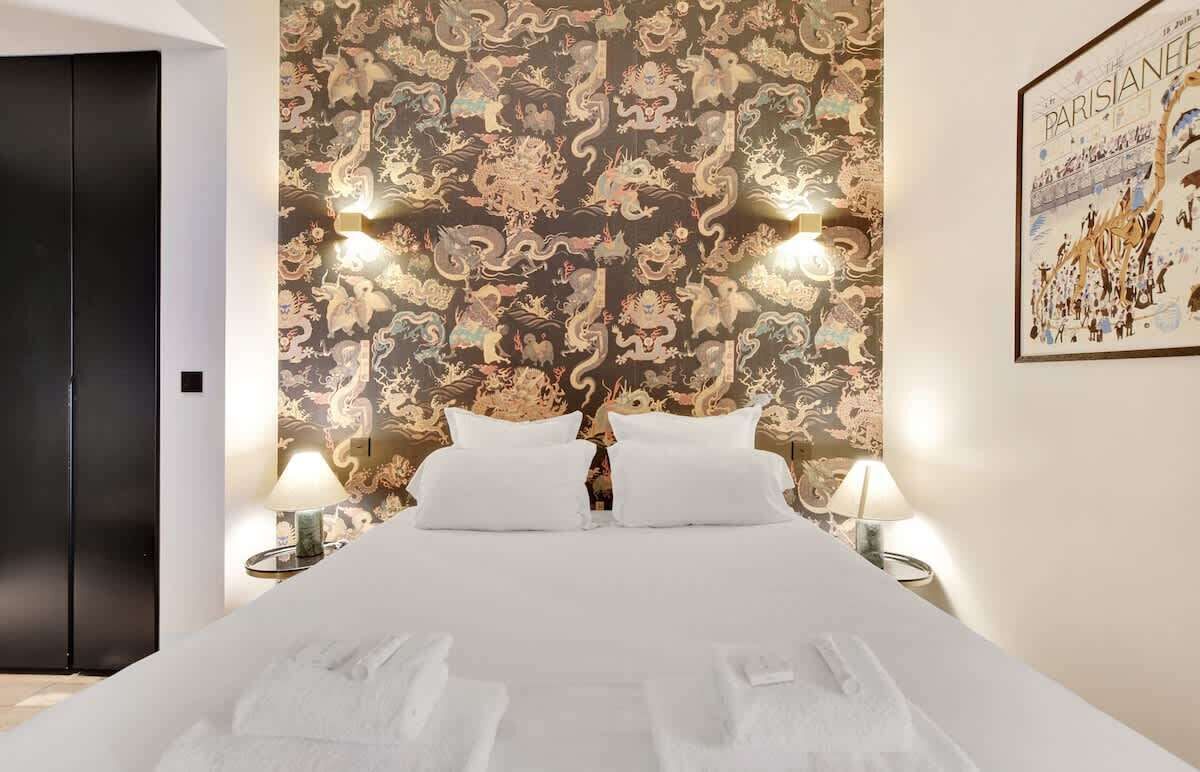 A hotel room with a large bed, two bedside lamps, a headboard with a dragon pattern, and a poster on the wall.