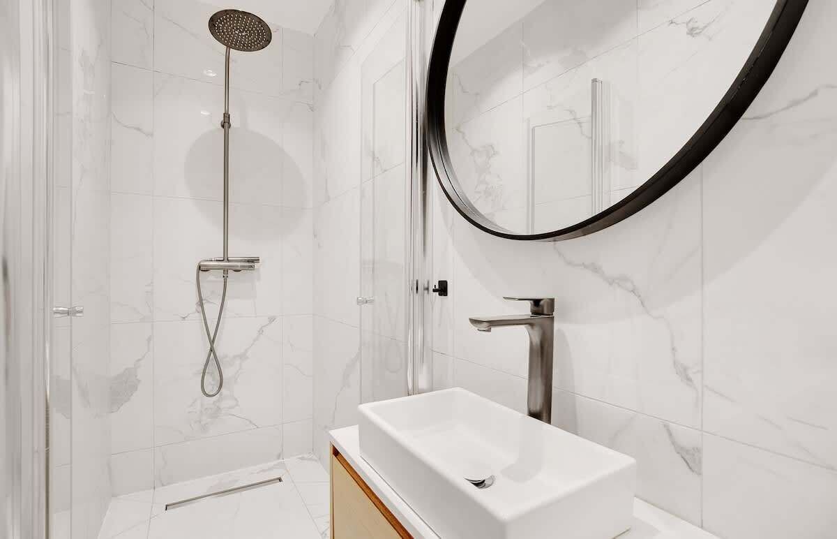 Een moderne badkamer met een douche in een glazen cabine, een wit wastafeltje en een grote spiegel.