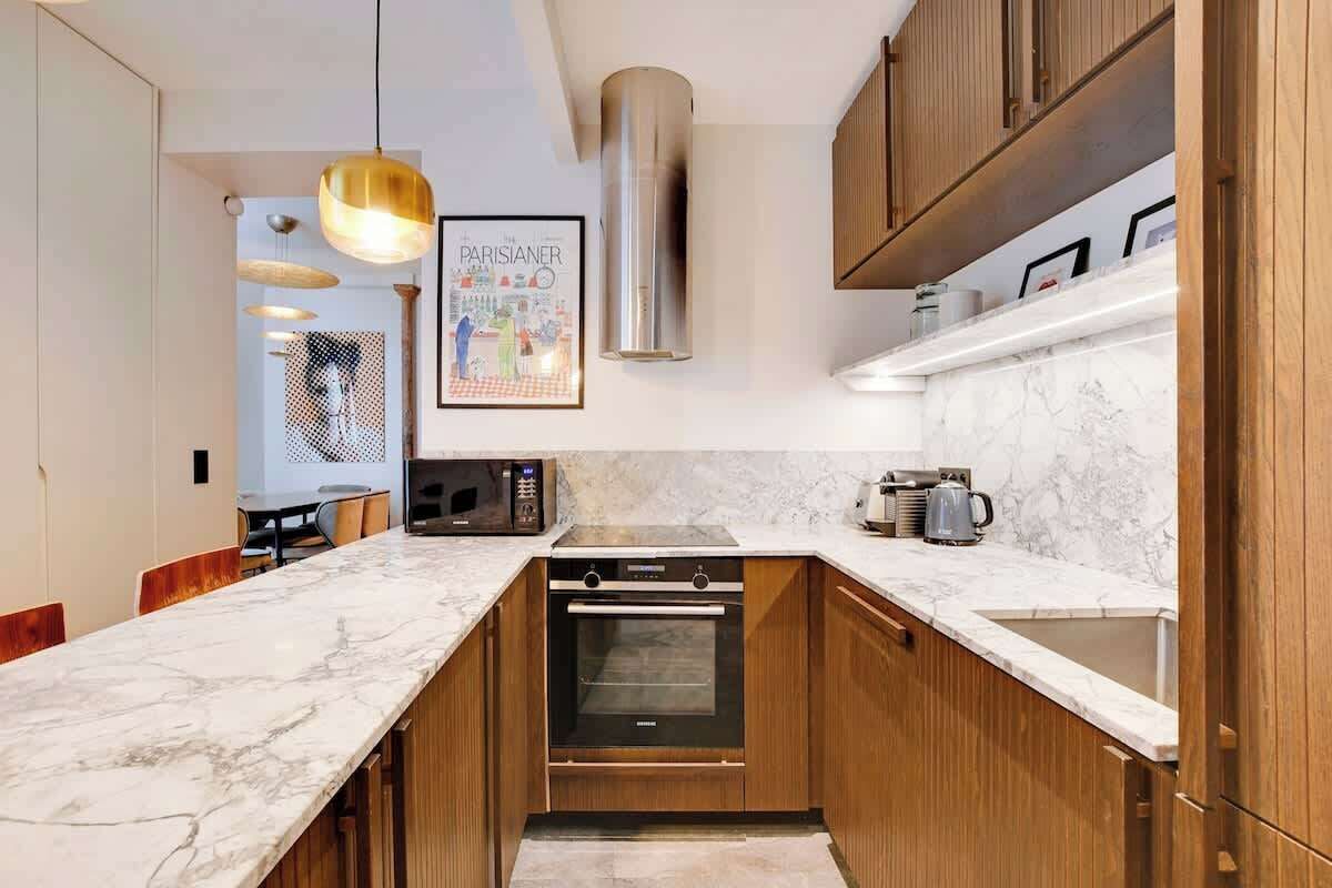 Eine moderne Küche mit Holzschränken, einer Marmorarbeitsplatte, einem eingebauten Backofen und Pendelleuchten.