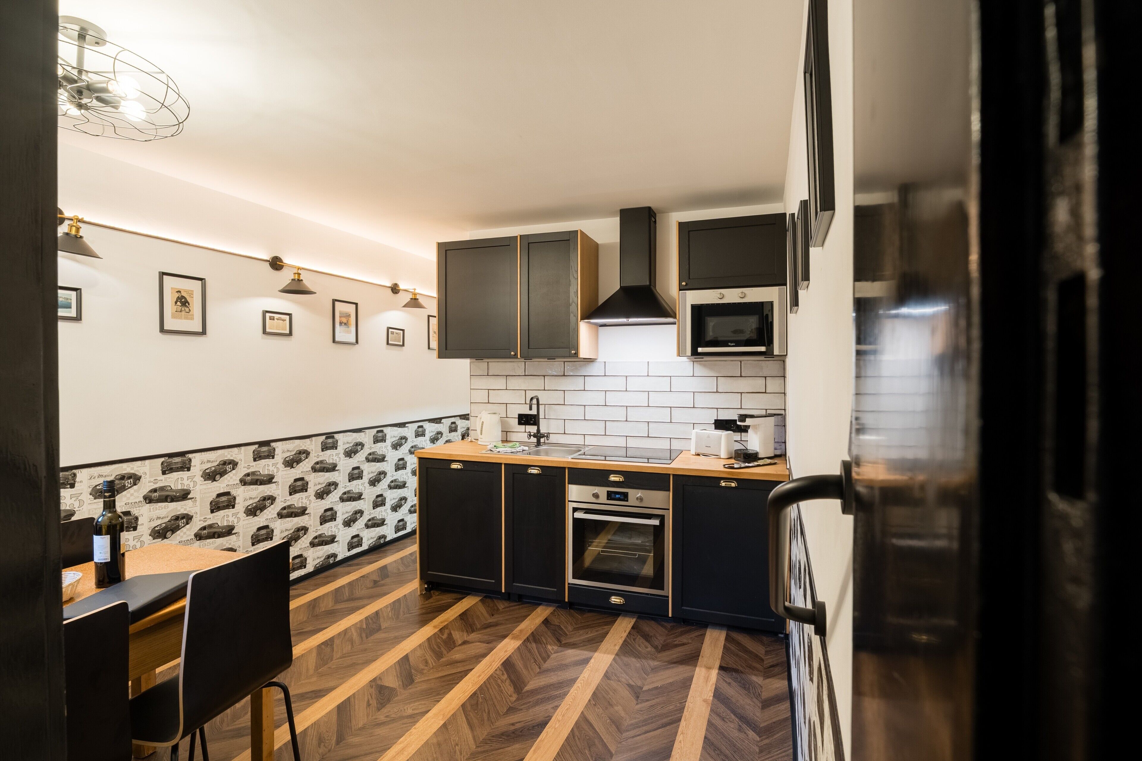 Une cuisine moderne avec un parquet en chevrons, des meubles de couleur noire, un four encastré et un four à micro-ondes.