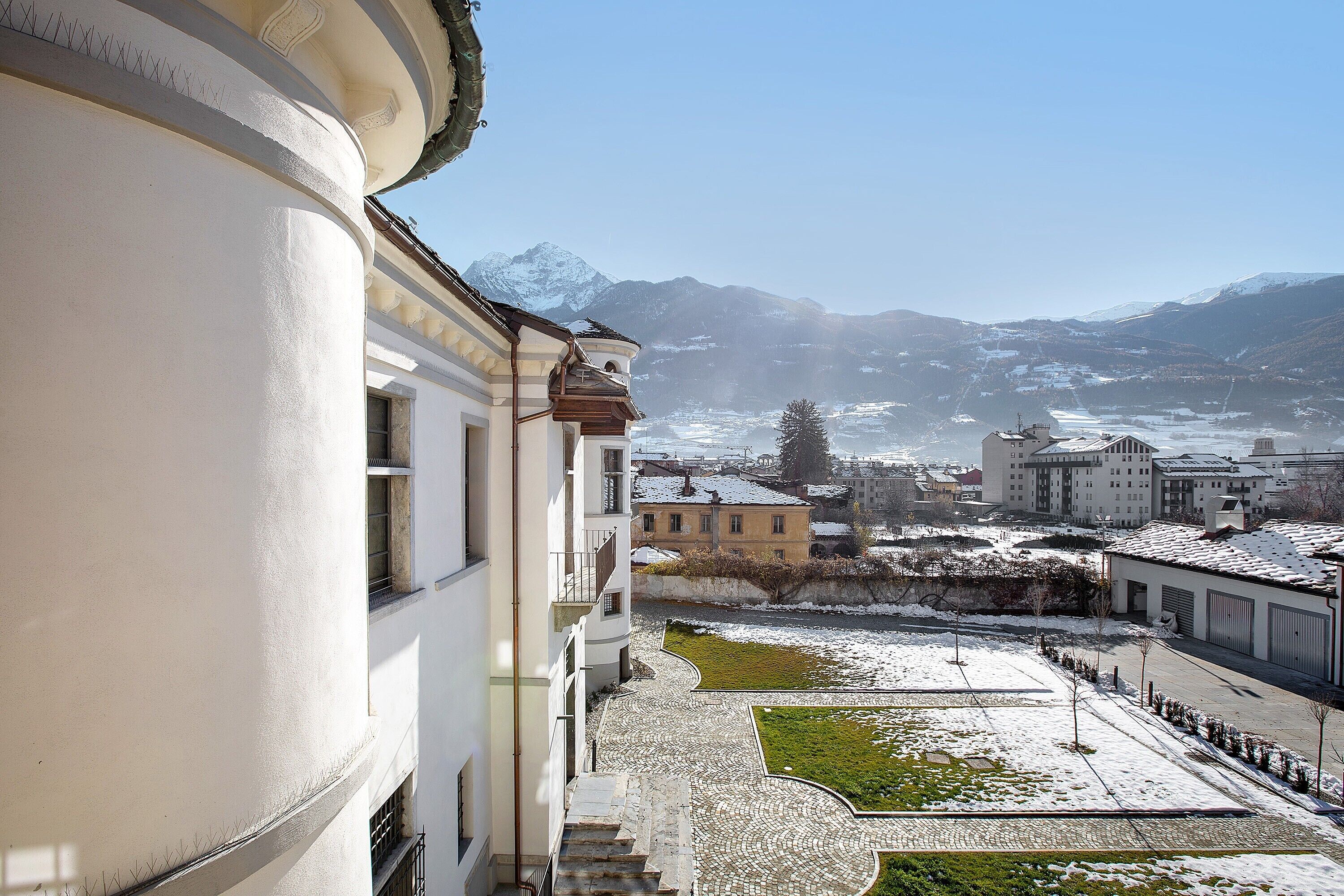 A building with a courtyard, a snow-covered landscape, and mountains in the background.