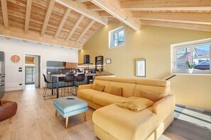 A spacious living area with a sofa, ottoman, and dining table. A kitchen is visible in the background. - La Maison De Ida - Grande Apartment with Mountain View, Wi-Fi and Air Conditioning (Aosta)