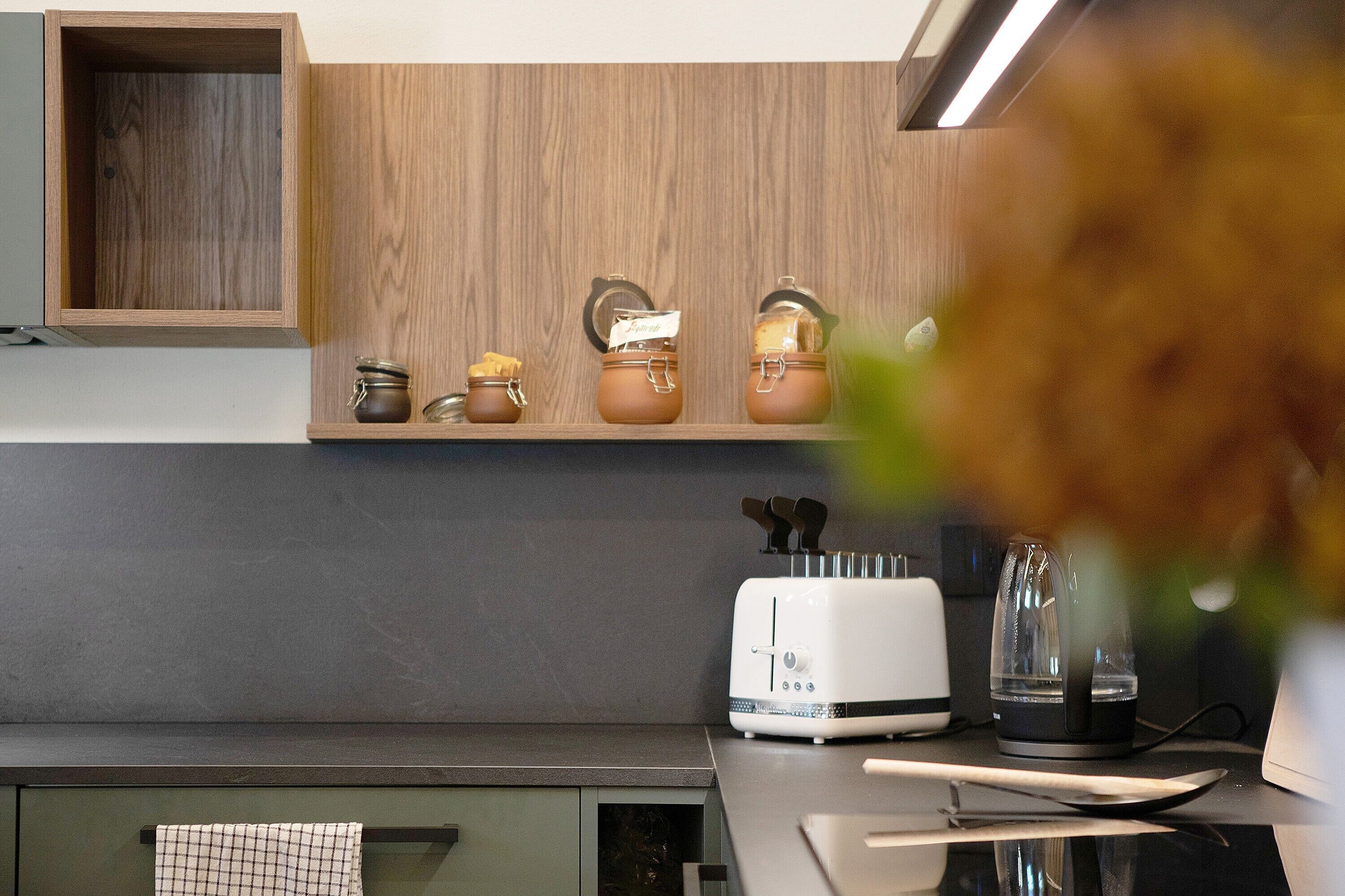 A kitchen with a wooden shelf, a toaster, a kettle, and jars.