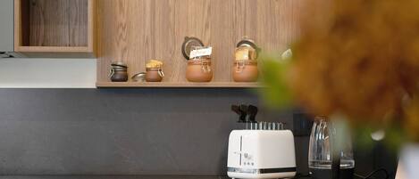 A kitchen with a wooden shelf, a toaster, a kettle, and jars.