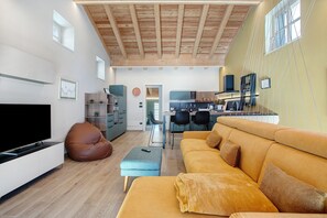 A modern living room with a sofa, ottoman, and television, a kitchen area, and a dining space. - La Maison De Ida - Grande Apartment with Mountain View, Wi-Fi and Air Conditioning (Aosta)