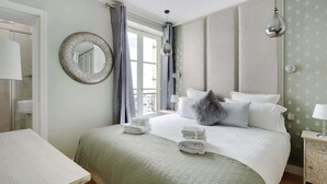 A hotel room with a bed, a round mirror, a window with curtains, a bedside table, and a lamp. - A Luxury 3-BR/3BA with A/C in Montmartre (Paris)