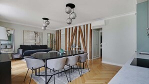 A modern kitchen with a marble countertop, a dining area with a large table and chairs, and a living room with a dark sofa and a painting on the wall. - A Luxury 3-BR/3BA with A/C in Montmartre (Paris)