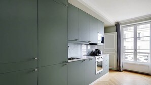 A modern kitchen with grey cabinets, a stove, and a window with a view of buildings. - A Luxury 3-BR/3BA with A/C in Montmartre (Paris)
