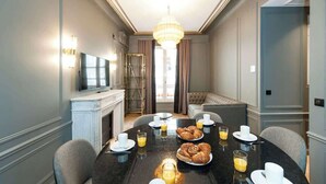 Uma área de refeições com uma mesa redonda posta para o café da manhã, incluindo croissants, suco de laranja e café.