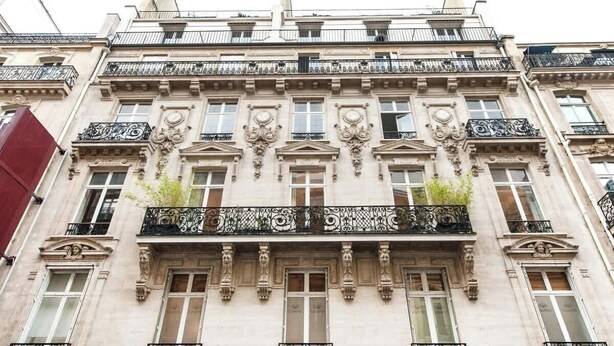 Um edifício com várias andares, varandas elaboradas e detalhes arquitetônicos clássicos.