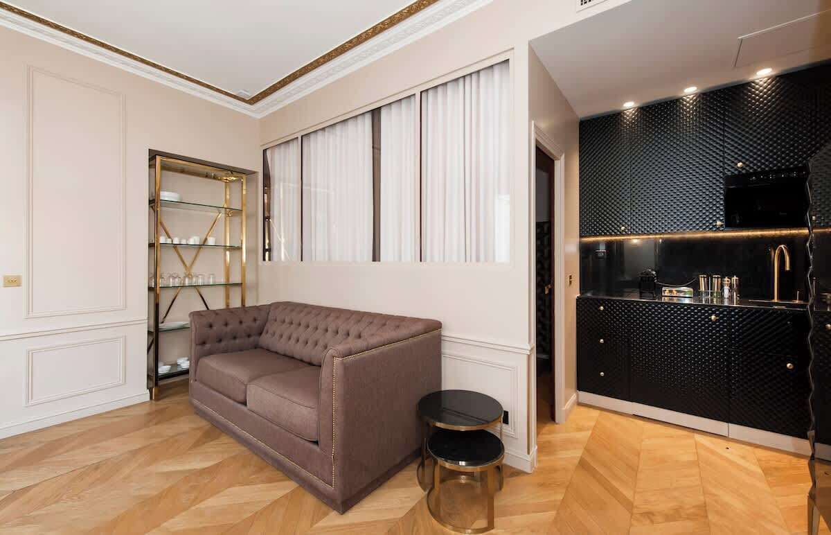 Una sala de estar moderna con un sofá marrón, un aparador de vidrio y una cocina oscura con un salpicadero texturizado.