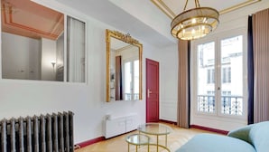 A modern hotel room with a large mirror, a chandelier, a radiator, and a view of the city through large windows. - A Sweet 2-BR nest in the Champs-Elysées (Paris)