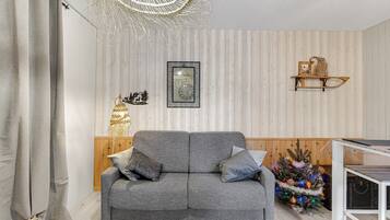 Ein graues Sofa mit Kissen, eine Wanduhr, eine Wanddekoration und ein kleiner Weihnachtsbaum.