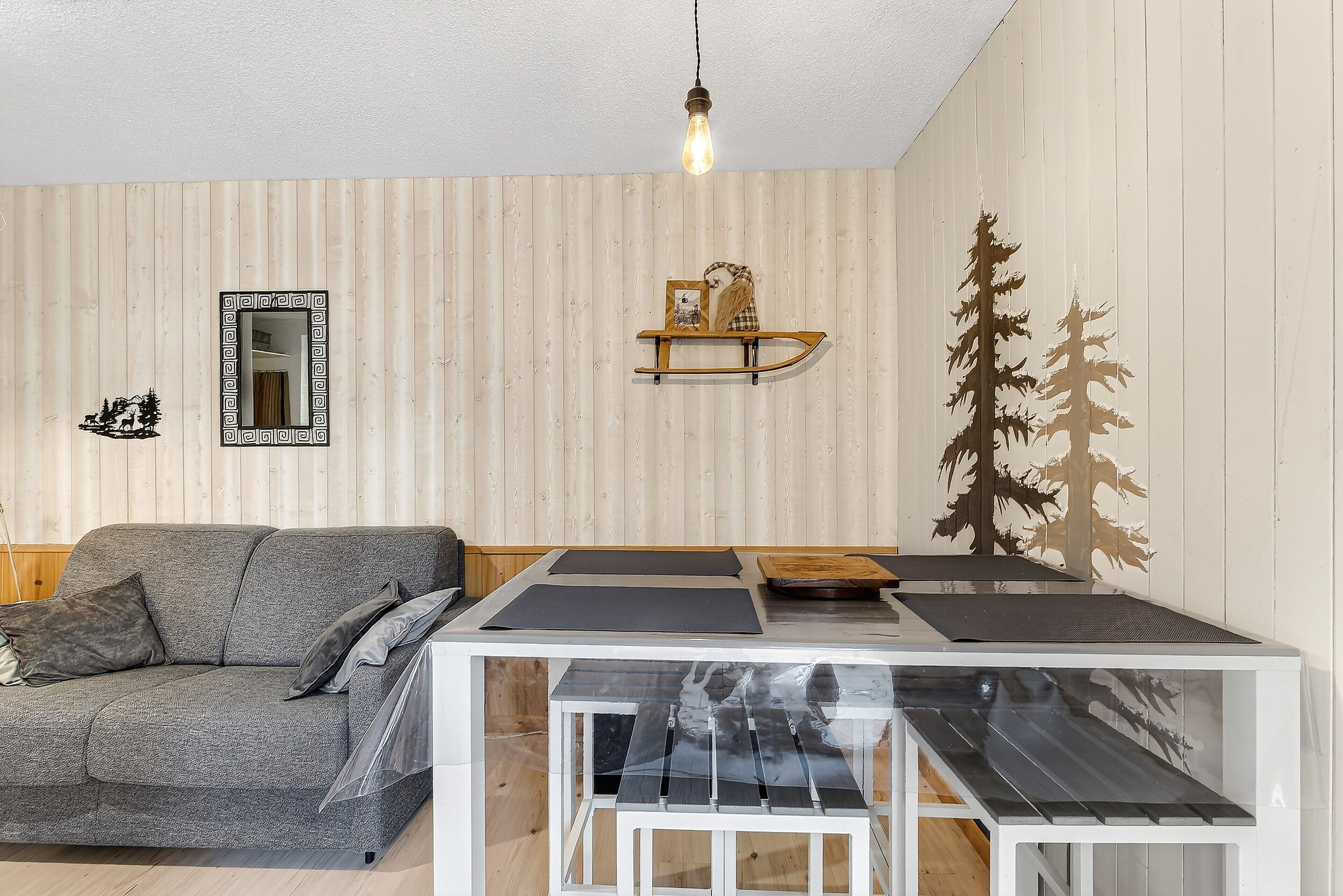 Une pièce avec un canapé gris, une petite table surmontée d’une armoire blanche, un miroir et un mur recouvert de lambris en bois verticaux.