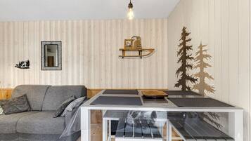 Une pièce avec un canapé gris, une petite table surmontée d’une armoire blanche, un miroir et un mur recouvert de lambris en bois verticaux.