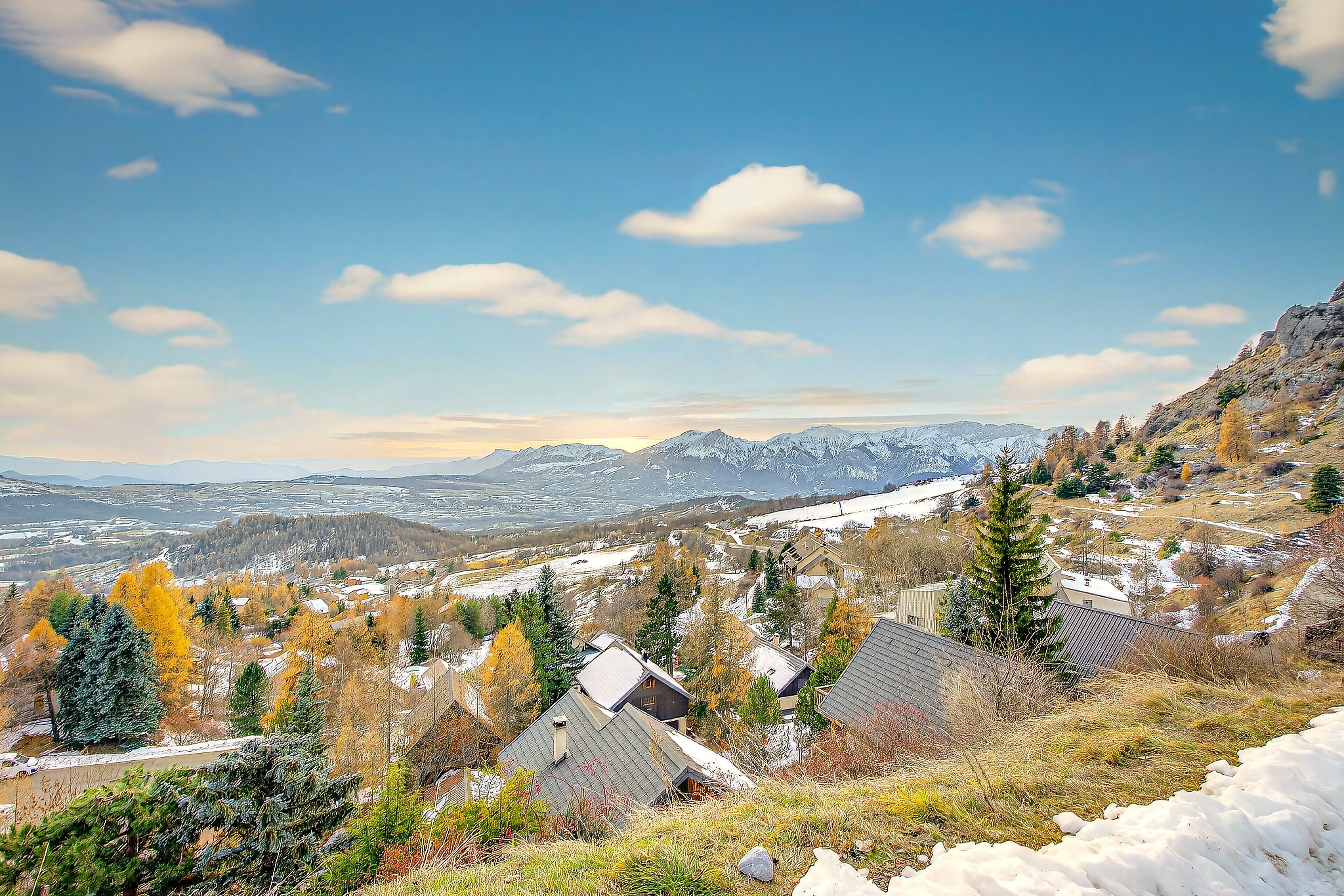 A mountainous landscape with houses, trees, and snow.