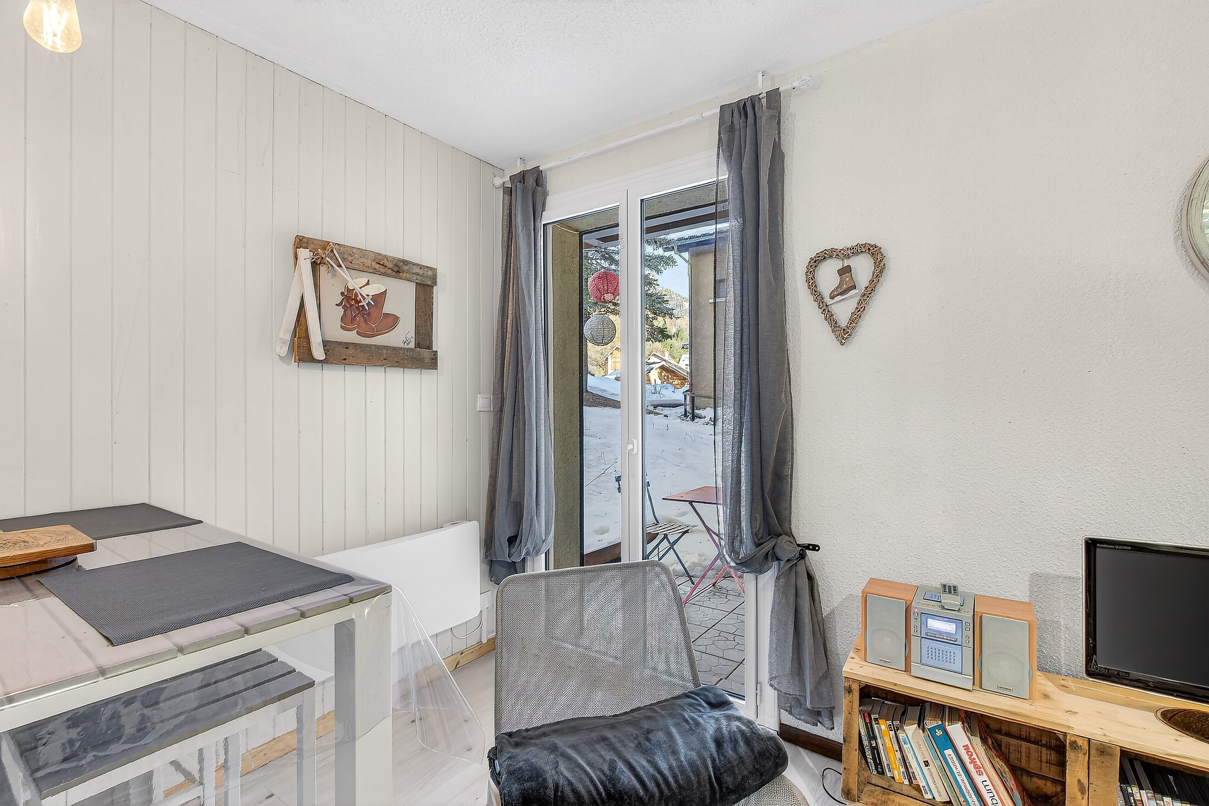 A room with a dining table, a cushioned chair, a bookshelf, a television, and a sliding glass door leading outside.