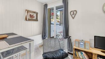 A room with a dining table, a cushioned chair, a bookshelf, a television, and a sliding glass door leading outside.