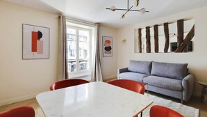 Un salon moderne avec un canapé gris, des fauteuils rouges, une table blanche et des œuvres d’art abstraites accrochées aux murs.