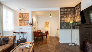 A living room with a herringbone floor, a fireplace, a television, and a brick wall bookshelf. - "Suite Gentleman" with King-Size Bed and Air Conditioning (Gengenbach)