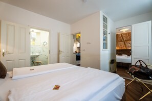 Habitación de hotel con una cama grande, un baño con espejo y vista a un muro de ladrillo a través de una puerta abierta.