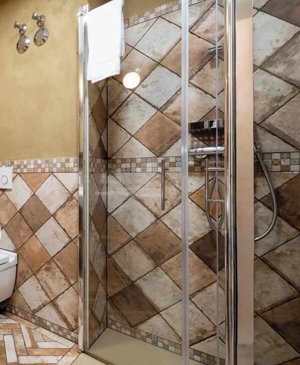Ducha con puerta de vidrio, paredes de azulejos y una toalla blanca colgada en la pared.