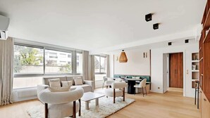 A modern living room with a sofa, chairs, a coffee table, and a dining area. There is a large window providing natural light and a view outside. - A Refined 3-BR/3BA in Trocadéro - Tour Eiffel (Paris)
