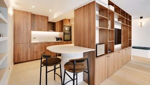 A modern kitchen with wooden cabinetry, a central island with stools, built-in appliances, and a wall-mounted TV. - A Refined 3-BR/3BA in Trocadéro - Tour Eiffel (Paris)