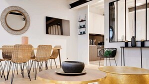 Een moderne woonkamer met rieten stoelen, een ronde gouden tafel en een grote spiegel aan de muur.
