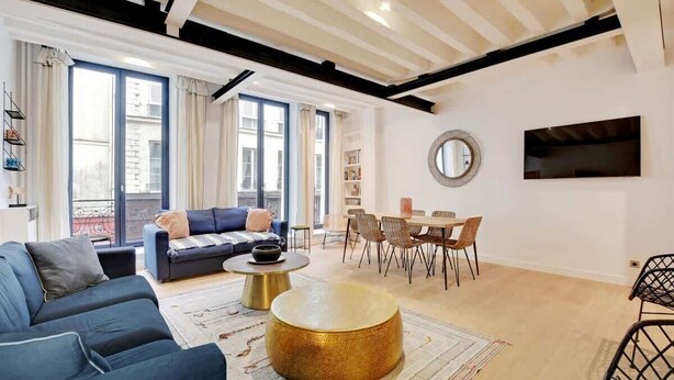 Een moderne woonkamer met een bank, salontafel, eethoek en grote ramen.