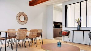 Een eetgedeelte met een ronde tafel, rieten stoelen, een spiegel en een vaas met bloemen.