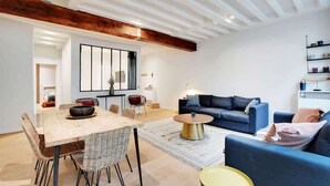 Een moderne woonkamer met een eethoek, met een blauwe bank, een houten eettafel en rieten stoelen.