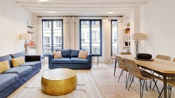 Un salon moderne avec un canapé bleu, une table basse ronde et un coin repas comprenant une table en bois et des chaises en osier.