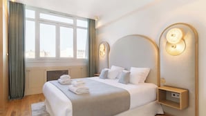 A modern hotel room with a large bed, a bedside table, and a view of the city through the window. - A Luxurious 3BR/3BA with A/C in Opéra-Bourse (Paris)